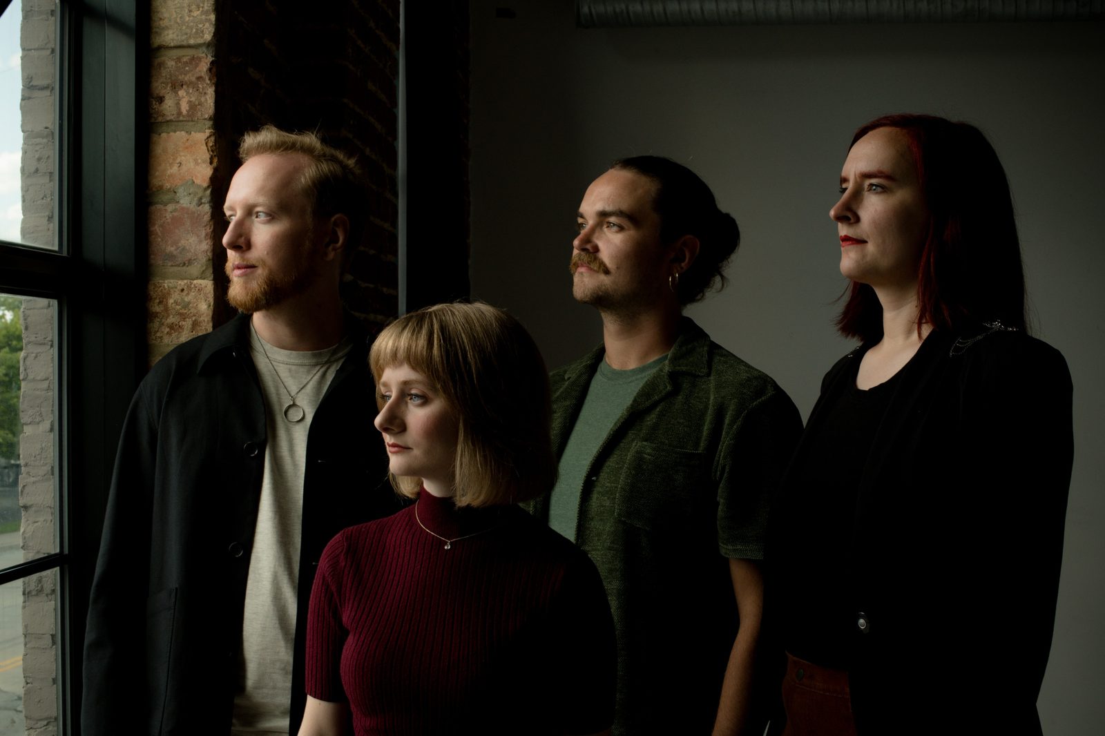 The four members of Anchorites standing together, lit warmly against a brick and window interior
